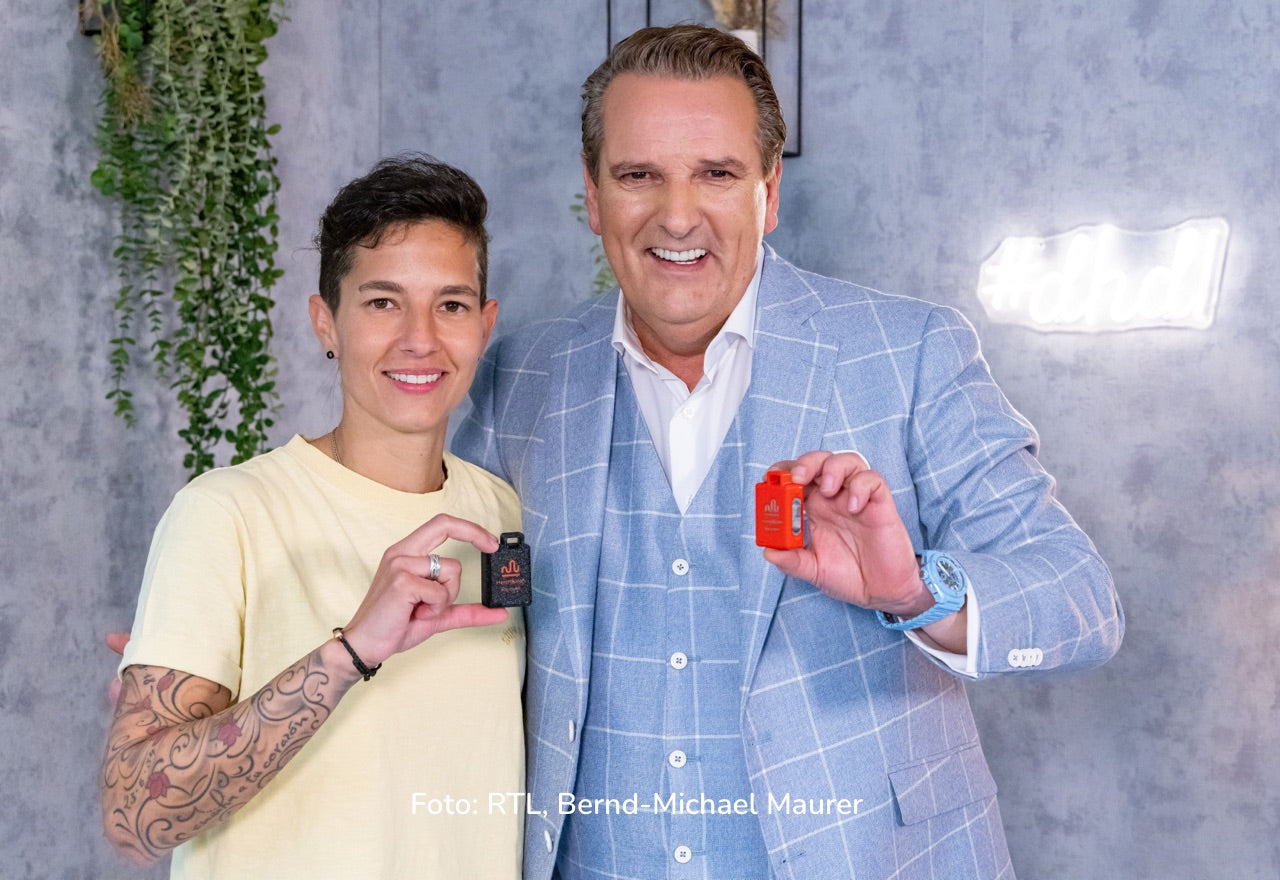 Foto: Zwei Personen posieren vor einer Wand; beide halten jeweils ein kleines Produkt/Objekt in der Hand; Text unten: „Foto: RTL, Bernd-Michael Maurer“.